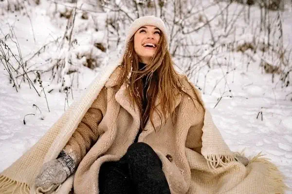 Une jeune femme assise dans la neige bien au chaud