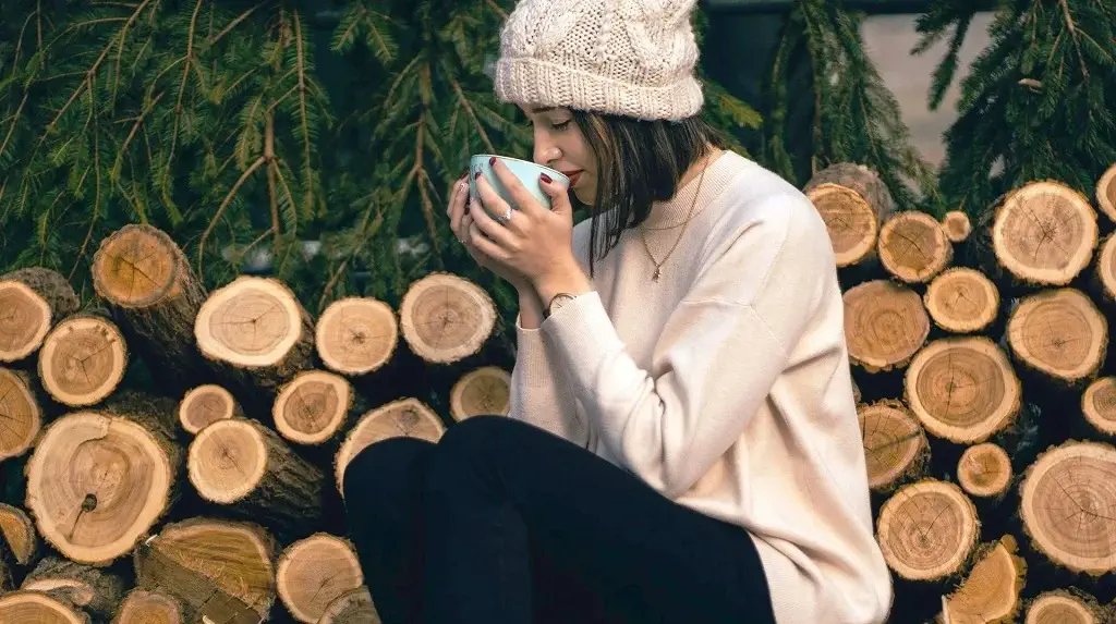une jeune femme assise dehors, une pile de bois à chauffer