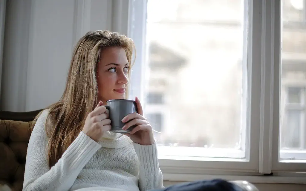 une jeune femme installée sur un canapé et tient un mug